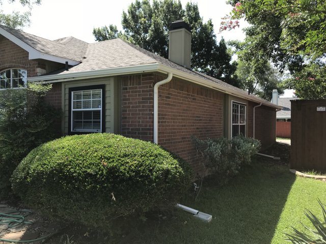 Exterior gutter and downspout beside a brick house.
